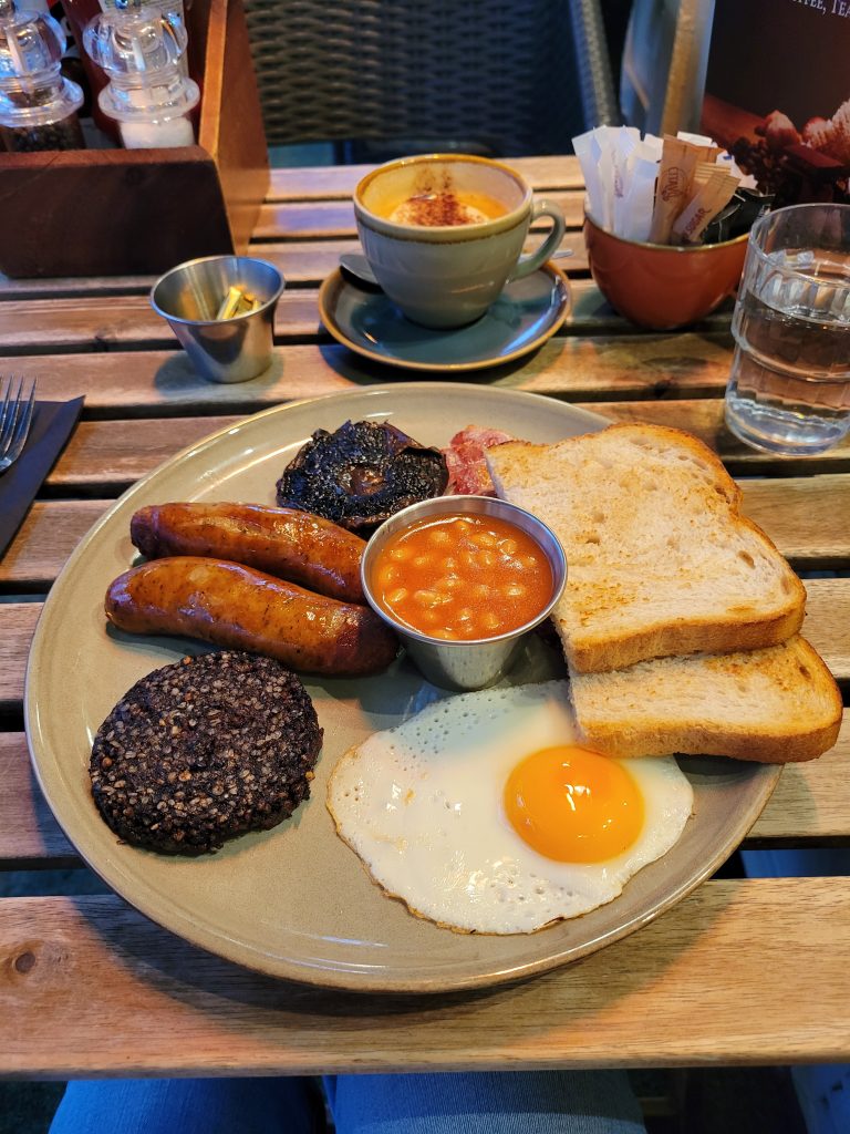 Photo of a cappuccino and a full Irish breakfast which includes fried eggs, sausage, black pudding, beans and toast.